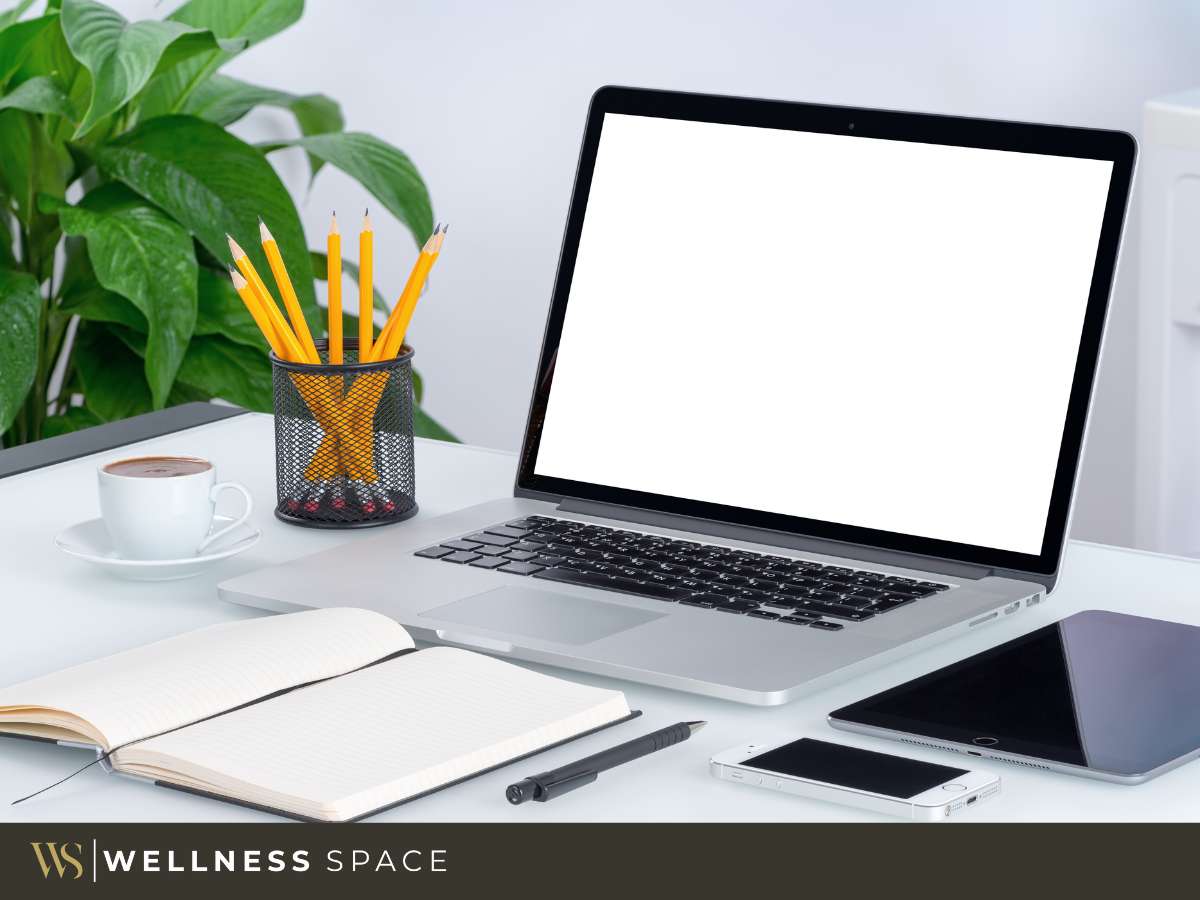 Therapy office rental setup with laptop, smartphone, coffee cup, and stationery on a desk, surrounded by lush green plants